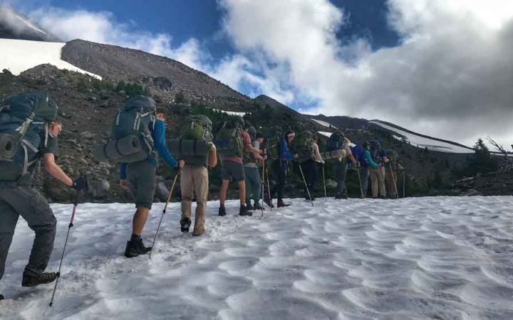 a group of backpacking students hike across a snowy field on an outward bound course